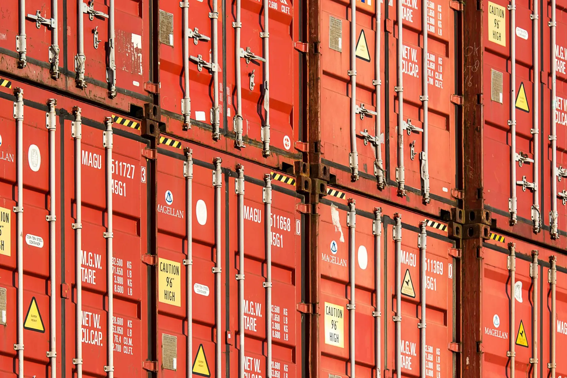 Stacked red shipping containers with door locking bars and load markings