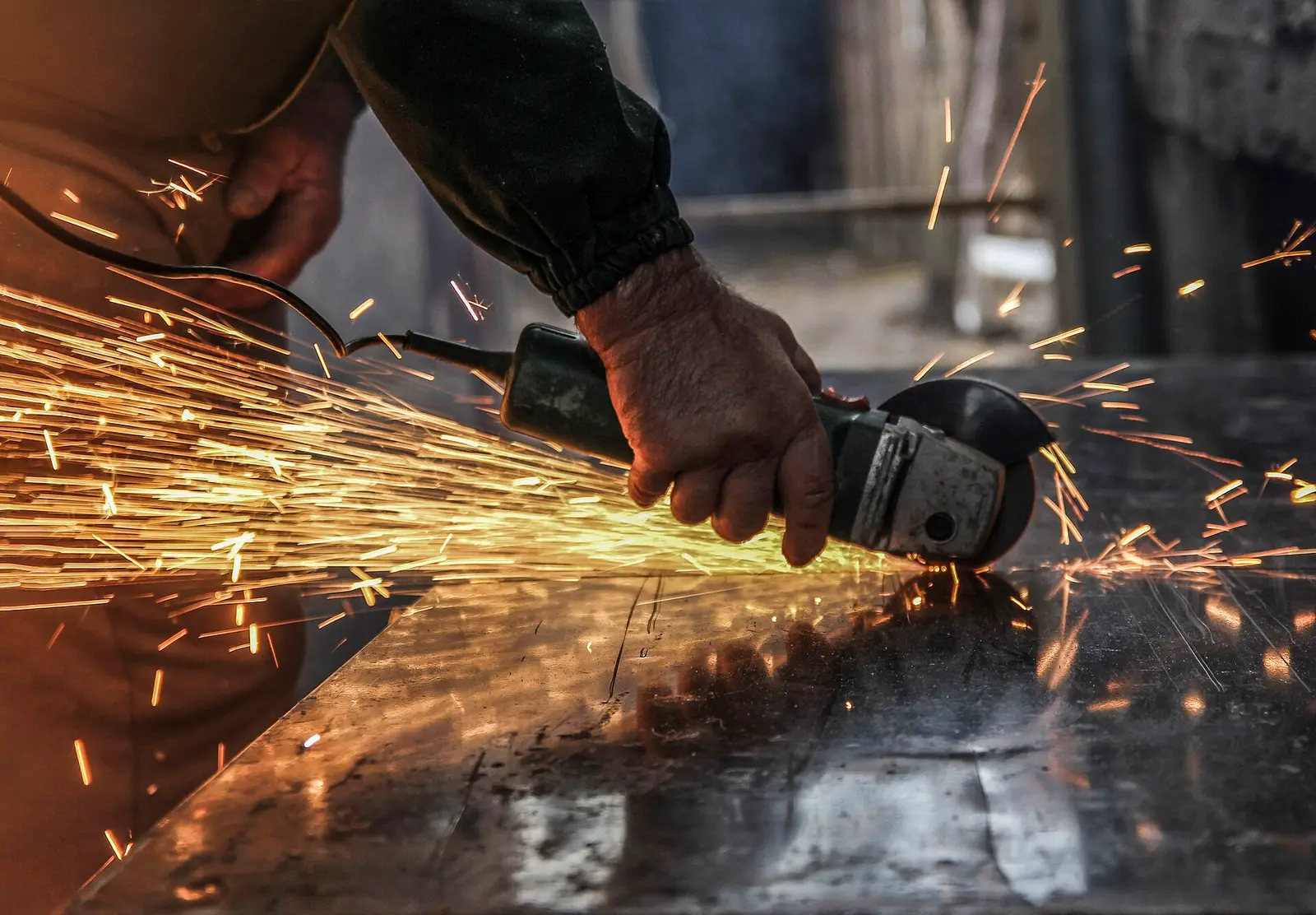 Close-up of a worker's hand holding an angle grinder cutting a steel sheet, throwing a spray of bright sparks