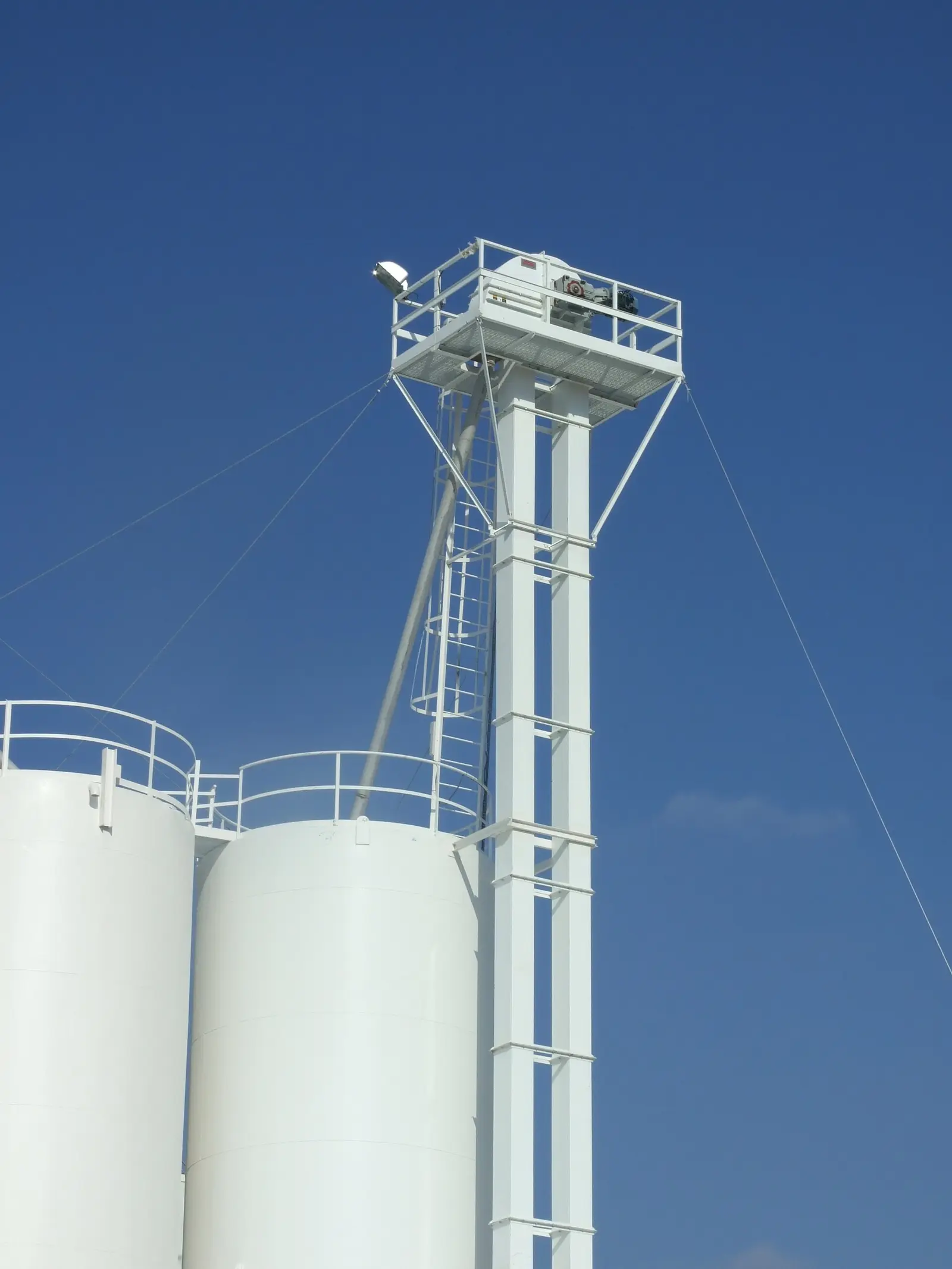 Belt bucket elevator, a tall enclosed vertical casing with head drive platform and discharge chute feeding storage silos