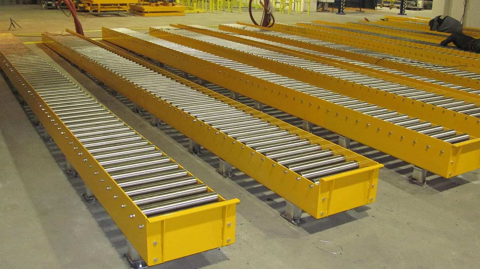 Roller conveyor sections, rows of free-turning steel rollers in yellow steel frames on a warehouse floor