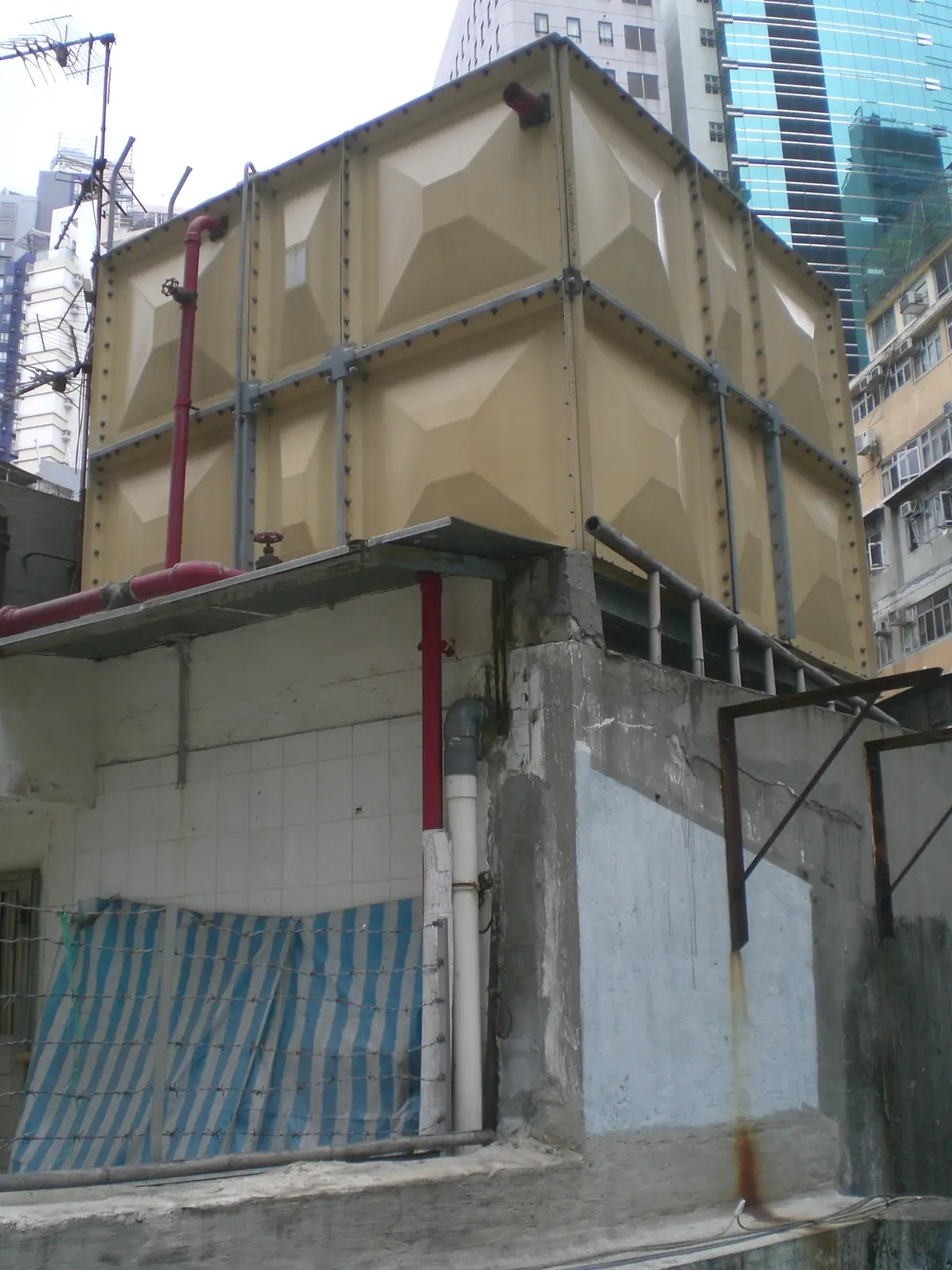 GRP sectional panel water storage tank, showing square moulded fibreglass panels bolted together with external steel tie-rods on a rooftop