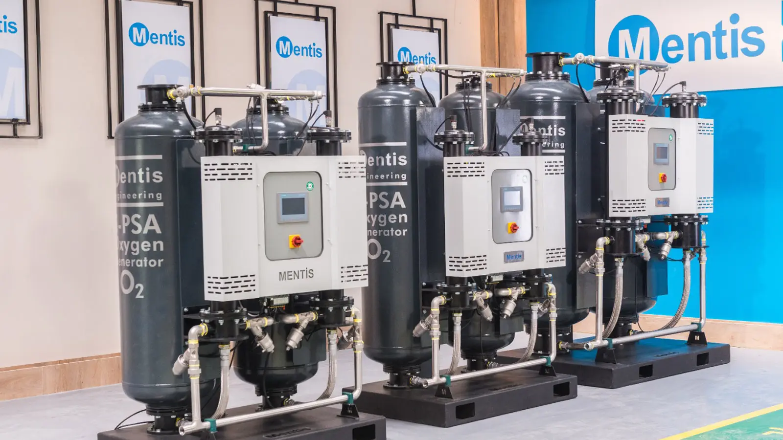 Three skid-mounted PSA oxygen generators, each with twin dark grey adsorber towers, a central control panel and stainless-steel piping, on a showroom floor